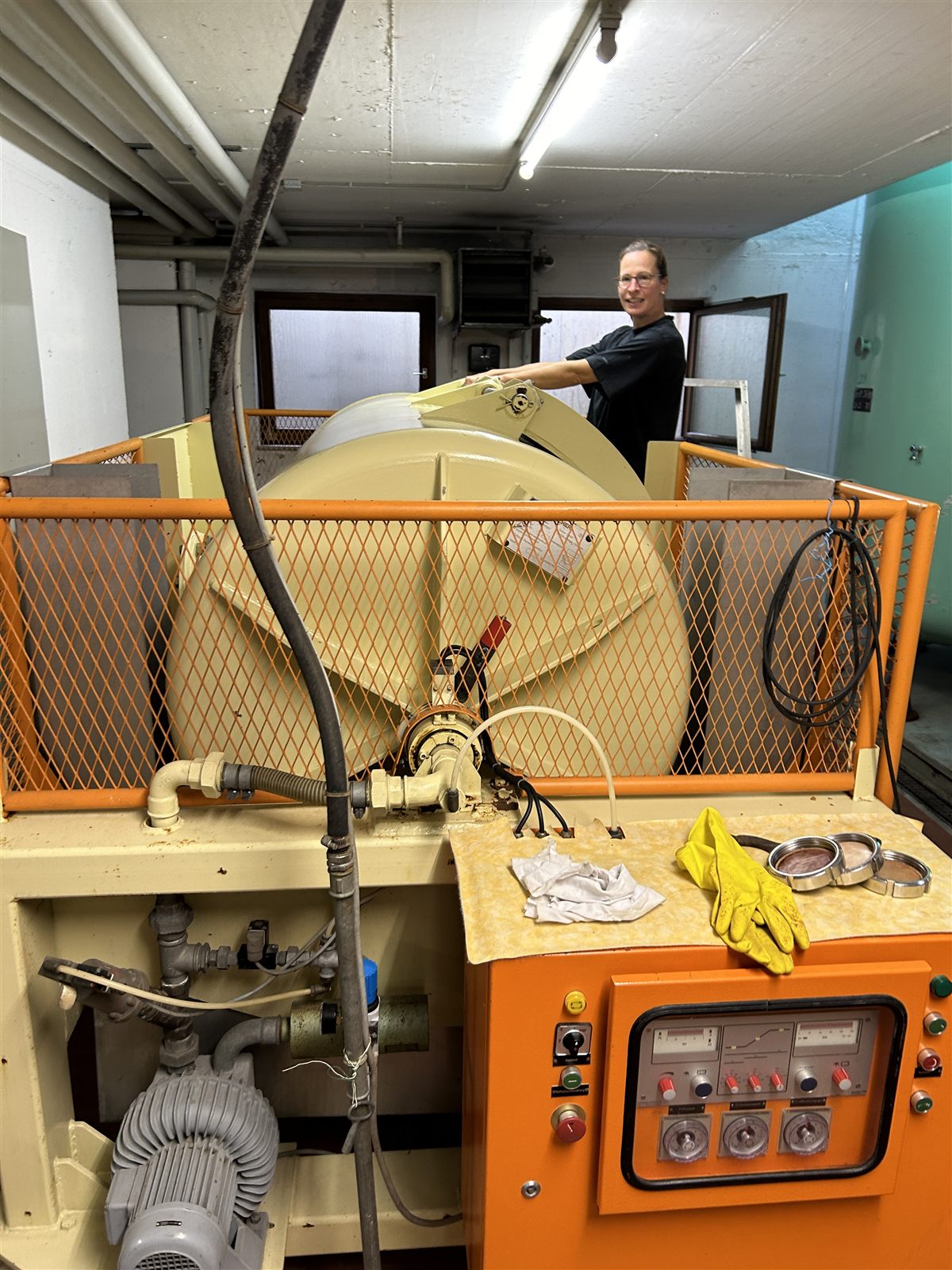 Die orange Weinpresse im Keller, davor Handschuhe und Werkzeug