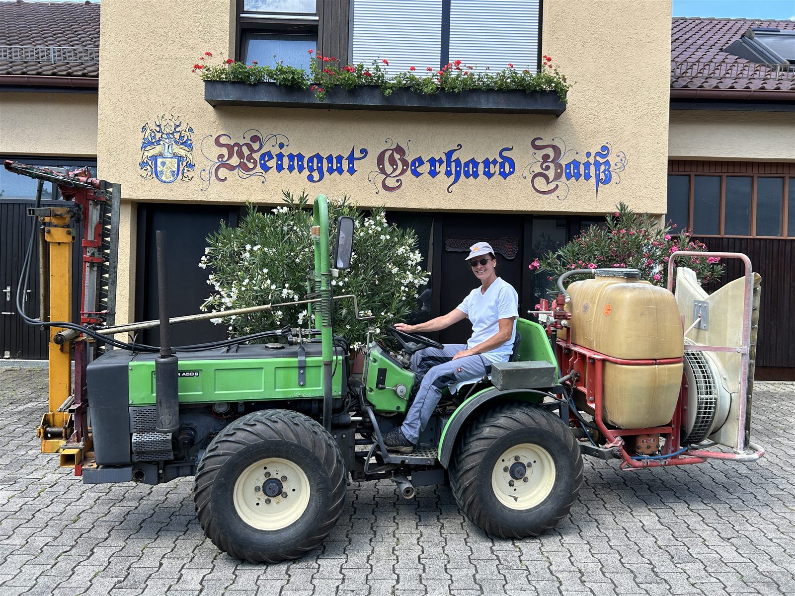 Ein grüner Traktor mit Anbaugerät vor der Fassade des Weinguts