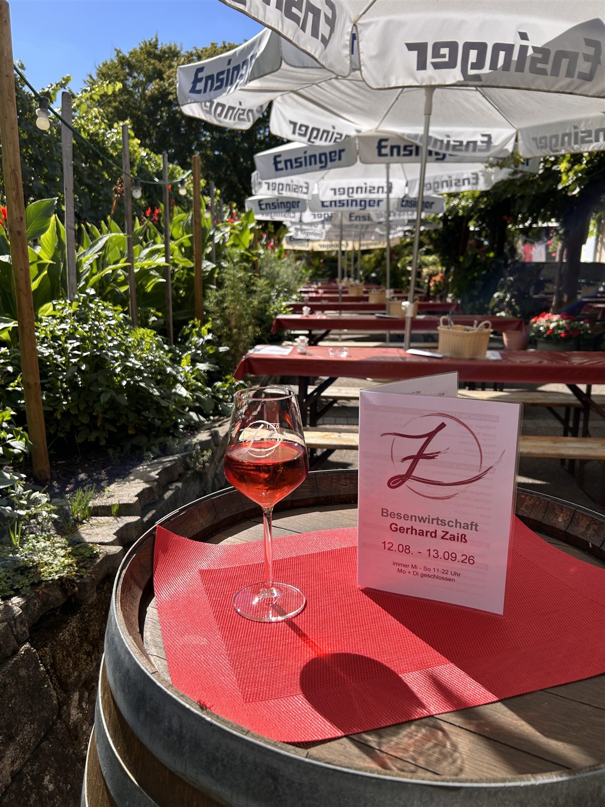 Ein Glas Rosé auf einem Weinfass, dahinter die Laube